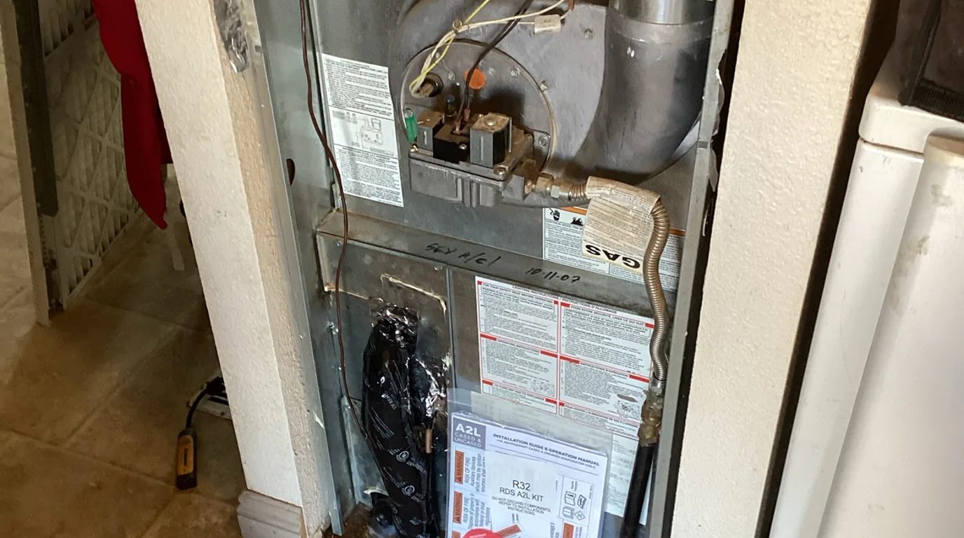 Gas furnace with the front panel open showing the gas valve and burner compartment during a service call