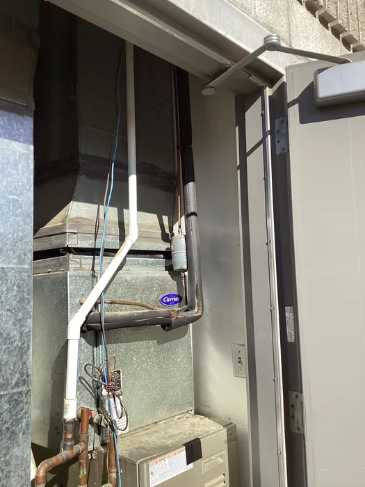 Open Carrier rooftop AC unit access panel showing insulated copper refrigerant lineset, electrical whip, and condensate piping on an Inland Empire roof.
