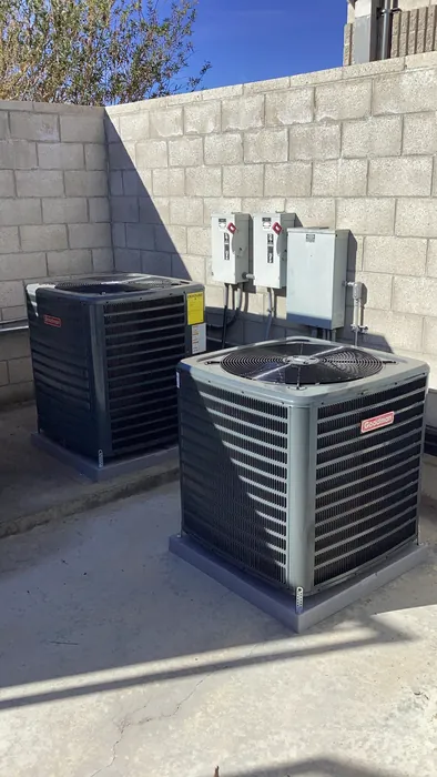 Two outdoor AC condenser units installed on pavers with wall mounted disconnect boxes under a blue Inland Empire sky.