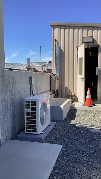 A newly installed outdoor AC condenser unit on a concrete pad beside a residential building with a clear High Desert sky.
