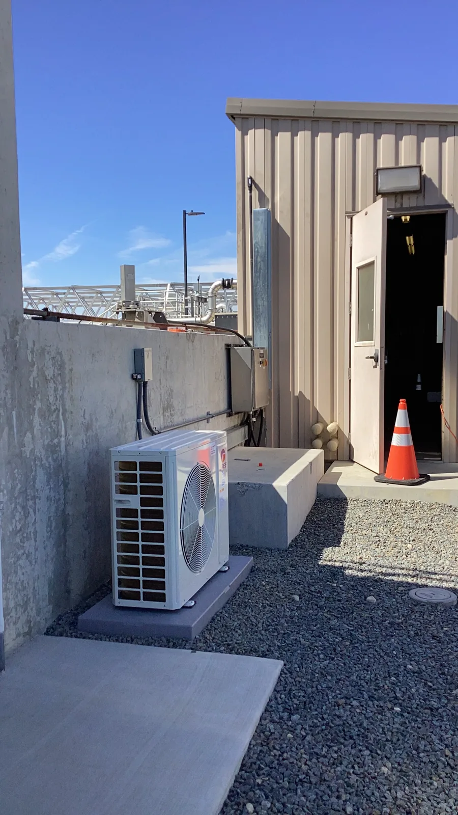 A newly installed outdoor AC condenser unit on a concrete pad beside a residential building with a clear High Desert sky.