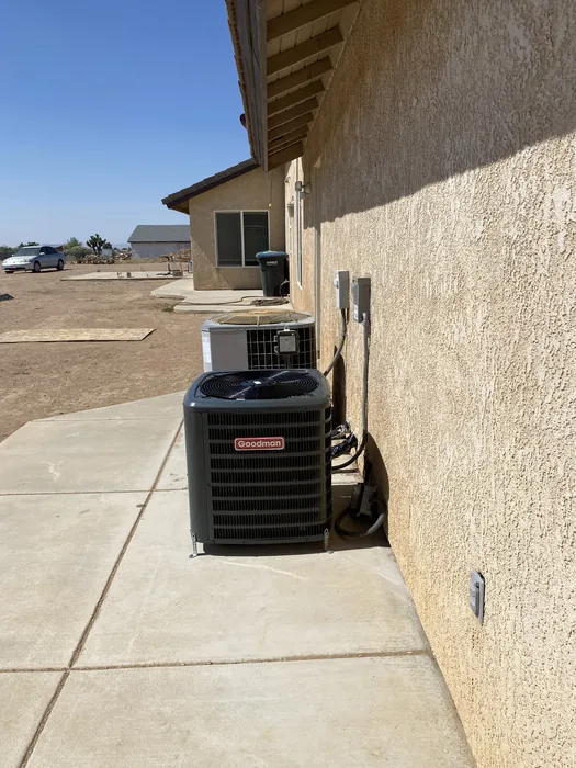 Goodman air conditioning condenser on a concrete pad beside a stucco home under clear High Desert skies in the Inland Empire.
