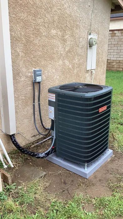 Goodman outdoor AC condenser unit set on a concrete pad with whip and disconnect box along the side yard of an Inland Empire home.