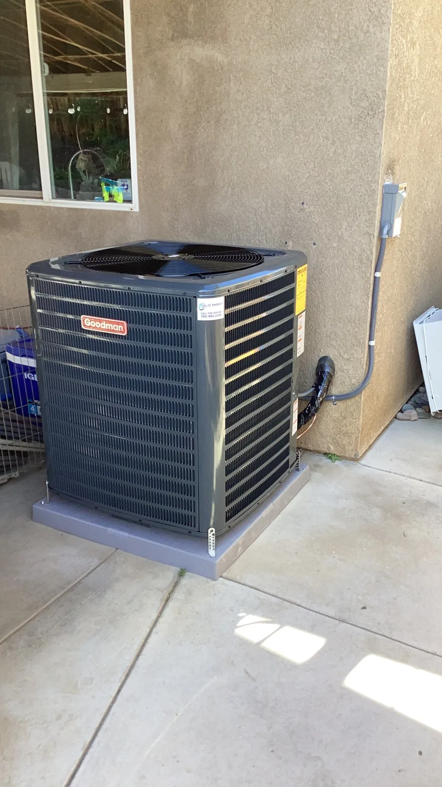 A Goodman residential AC condenser unit installed on a concrete pad along a home exterior in the High Desert.