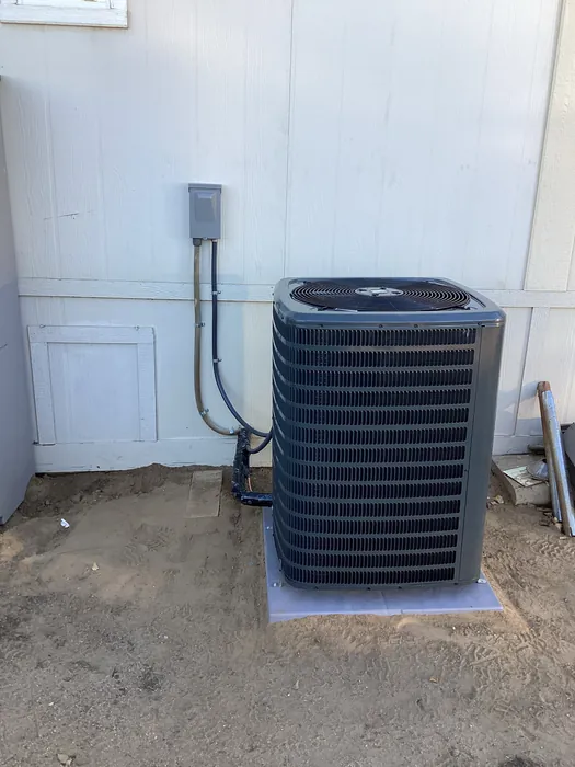 Outdoor air conditioning condenser unit installed against a home exterior wall with copper line set and electrical disconnect box.