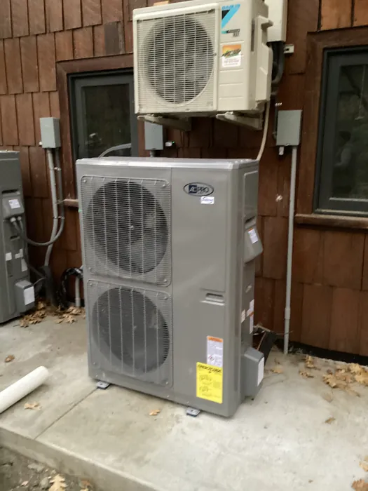 Outdoor AC condensing unit beside a Daikin mini split condenser mounted on a wood-sided home in the Inland Empire.