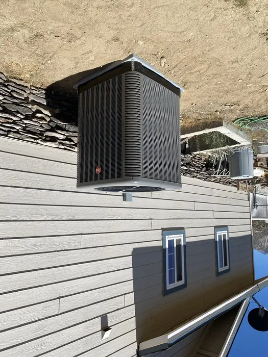 Newly installed Rheem air conditioning condenser on a gravel pad beside a High Desert home in the Inland Empire.
