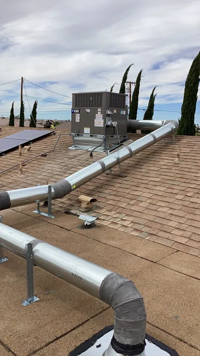 Rooftop-mounted packaged AC condenser unit with freshly installed metal supply and return duct runs across composition shingles on a High Desert home.