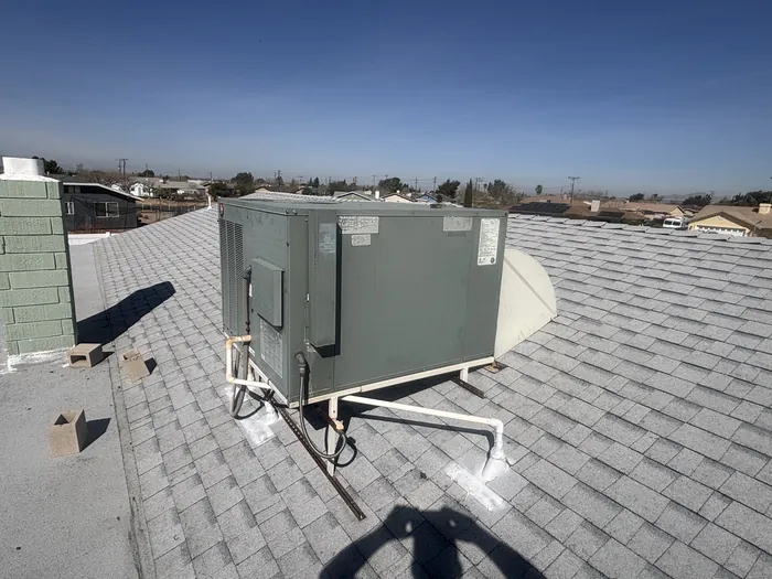 Gray rooftop package gas-pack HVAC unit set on a shingle roof with a High Desert neighborhood and clear sky in the background.