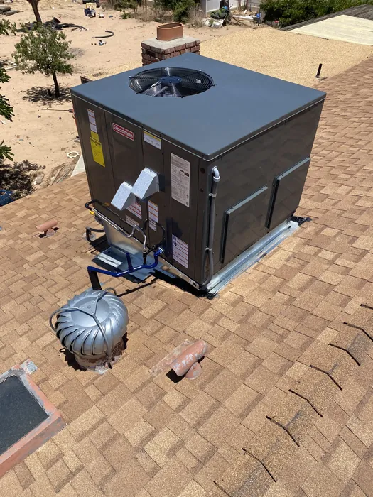 Rooftop packaged HVAC unit set on a composition shingle roof beside a turbine vent at a High Desert property.