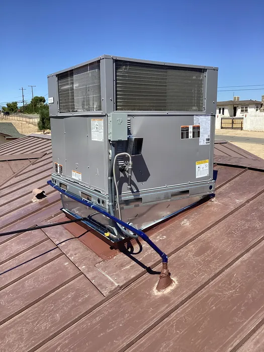 A freshly installed rooftop packaged AC condenser with exposed coil and new line set on a metal roof in the High Desert.