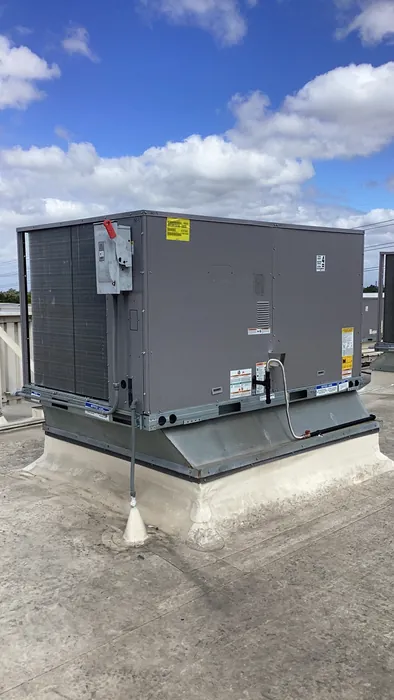 A gray commercial packaged gas pack HVAC unit installed on a flat rooftop curb under a blue sky.