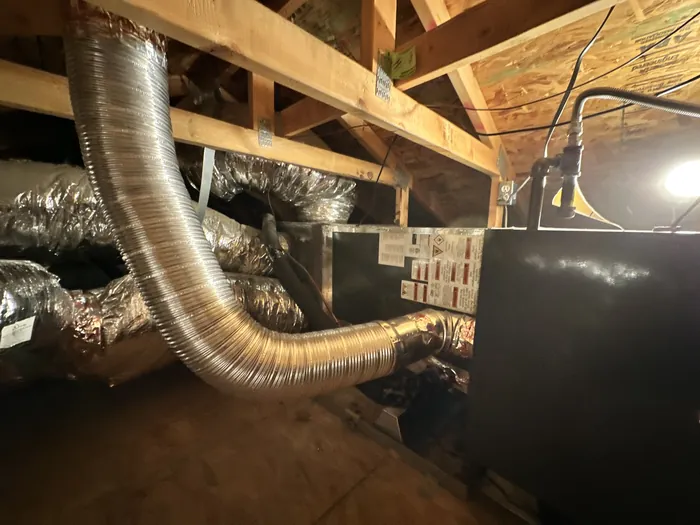 Attic HVAC layout with multiple insulated flex duct branches and aluminum flue venting routed to a sheet-metal air handler under the roof framing.