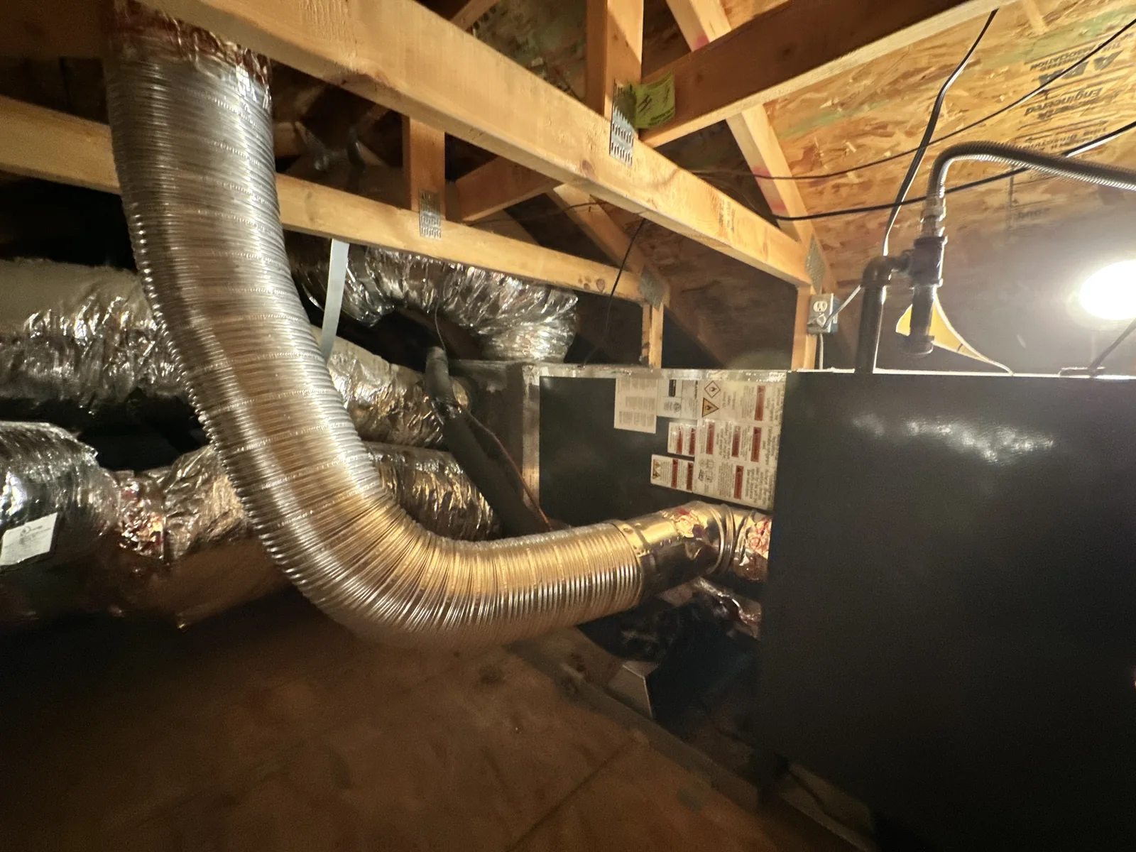 Attic HVAC layout with multiple insulated flex duct branches and aluminum flue venting routed to a sheet-metal air handler under the roof framing.