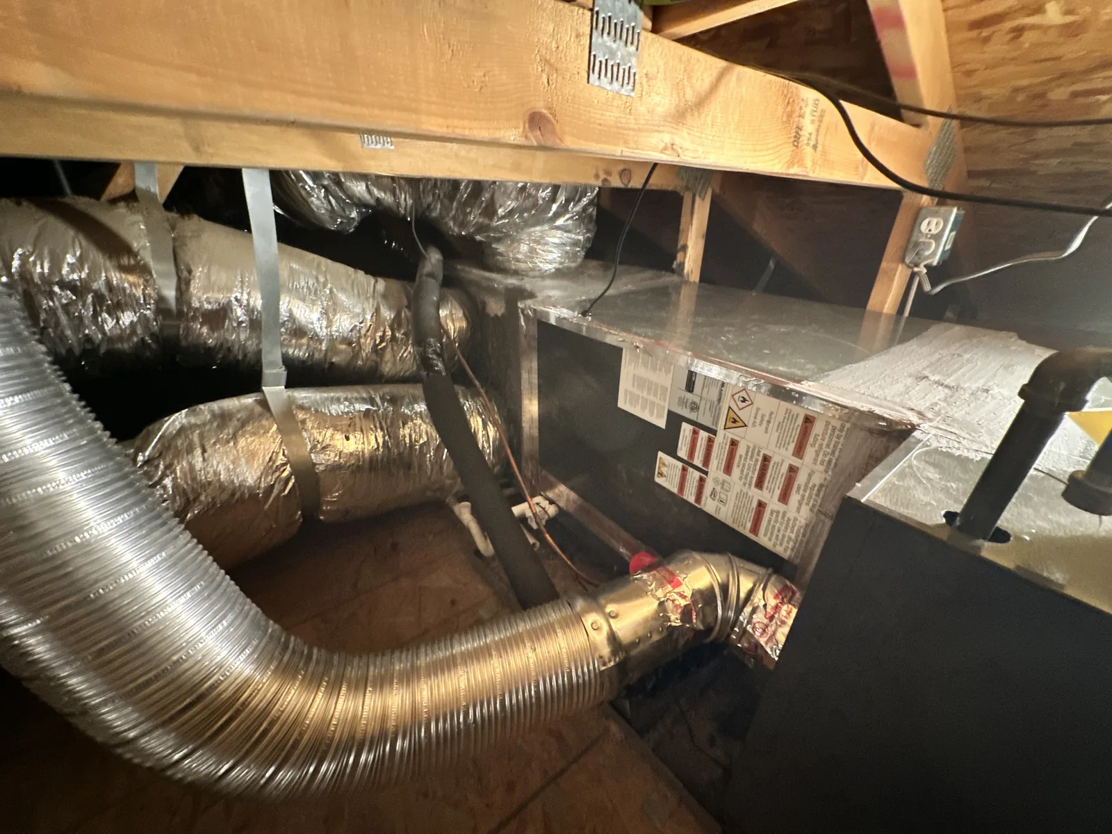 Attic ductwork showing insulated flex duct runs, a sheet-metal plenum, and a flexible aluminum flue pipe connected to the air handler.