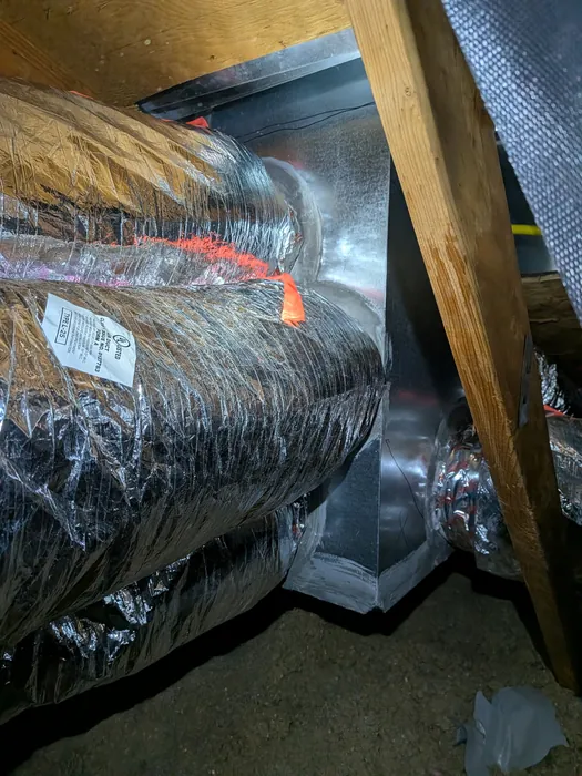 Insulated flexible HVAC ductwork connected to a sheet metal supply plenum in a dim High Desert attic.