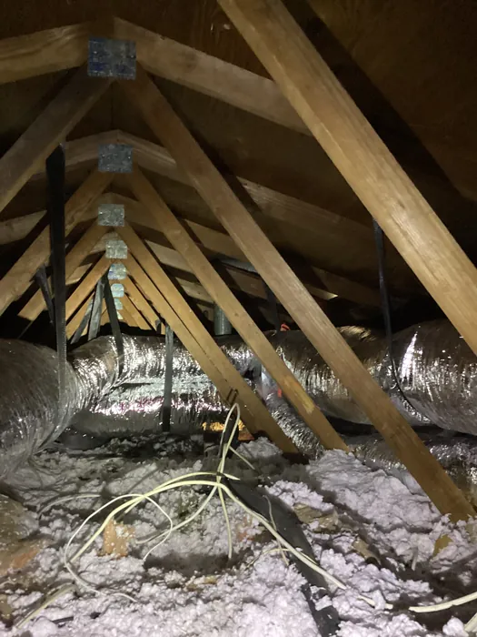 Flexible silver HVAC ducts routed through an attic between wood roof trusses above blown-in insulation in a High Desert home.