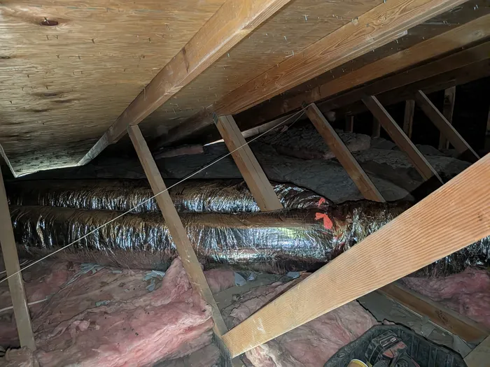 Insulated flexible duct runs threaded between attic rafters over blown insulation in an Inland Empire home.