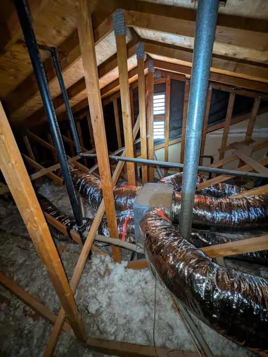 Insulated flex ductwork branching off a metal supply plenum between wood framing in an attic.