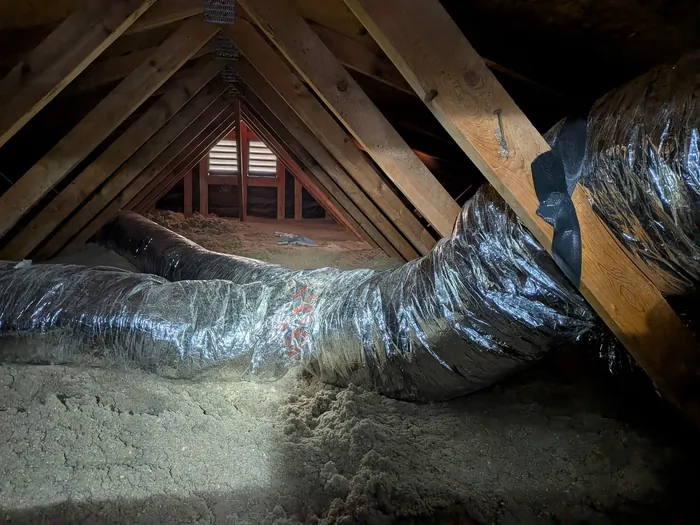 Insulated flex duct runs spanning the rafters of an Inland Empire home attic near a gable vent.
