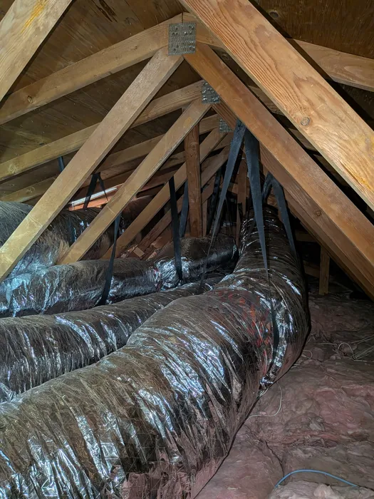 Large insulated flexible duct trunk running along the attic rafters above fiberglass insulation in an Inland Empire home.