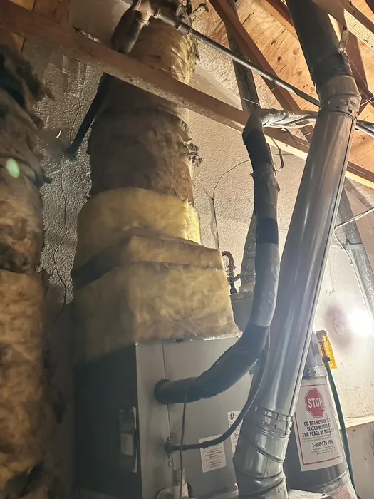 Insulated supply trunk ductwork and rigid metal flue piping running through a residential attic above an air handler in the High Desert.