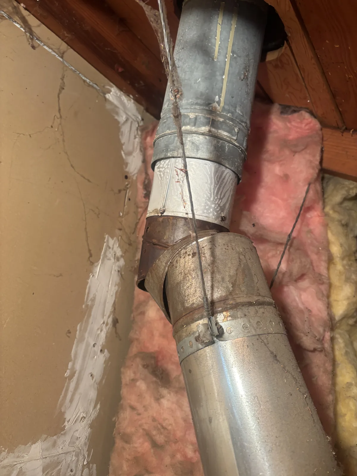 Galvanized sheet metal duct sections joined at a collar fitting surrounded by insulation in an attic HVAC system.