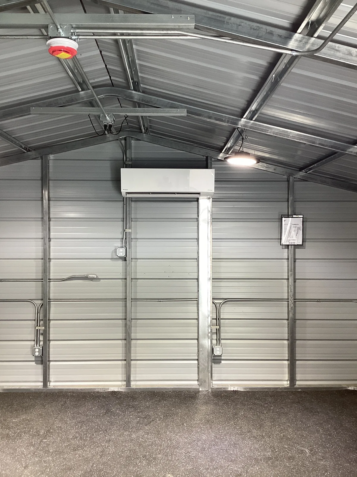 Overhead HVAC piping and air handler rough-in running across the steel framing of a metal commercial building interior.