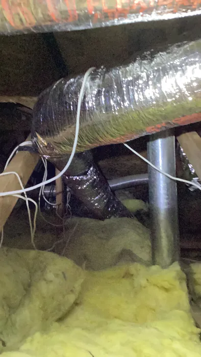 Flexible duct connected to a sheet-metal trunk beside yellow batt insulation in a tight crawlspace under a home.