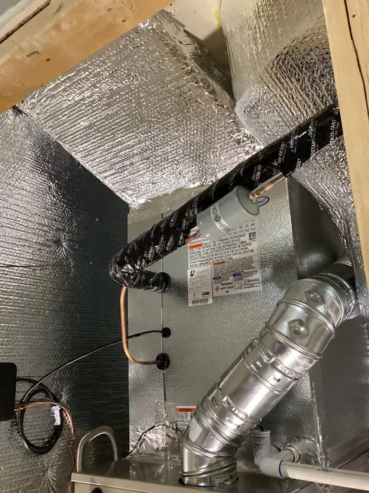 Carrier air handler unit with taped refrigerant lineset, copper drain, and galvanized supply duct mounted over reflective insulation in an Inland Empire home