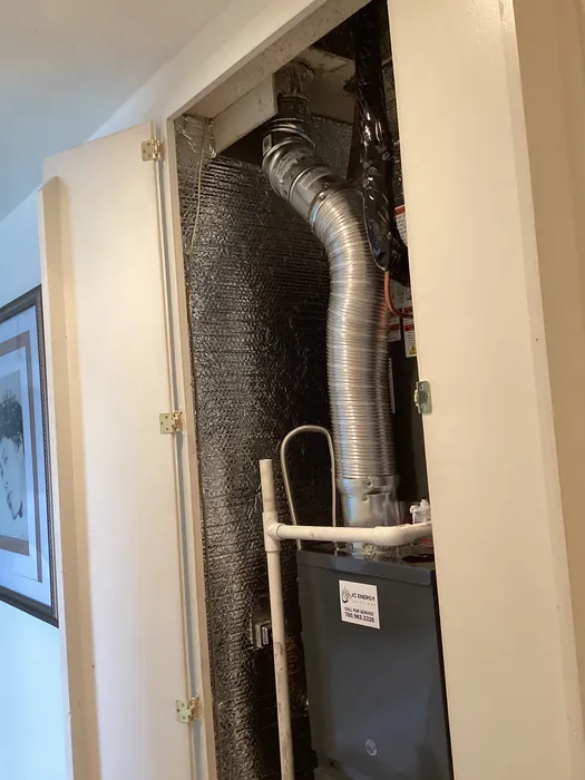 Closet-mounted air handler with a flexible metal flue duct and a JC Energy service sticker visible behind an access panel in a High Desert home.