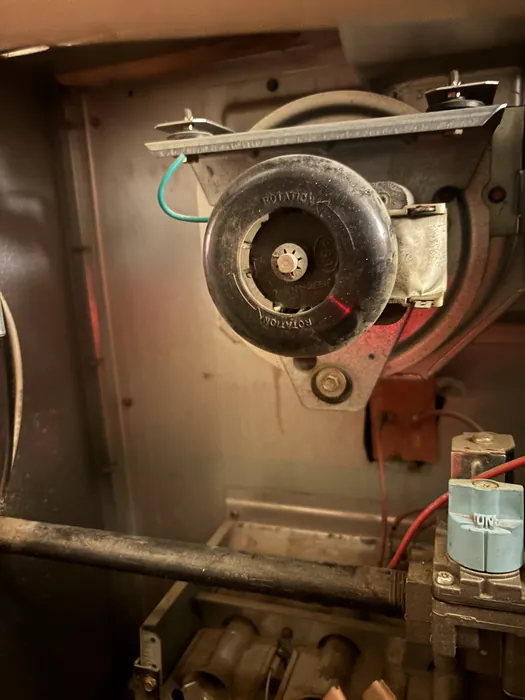 Close-up inside a furnace cabinet showing the round draft inducer blower motor and gas valve with wiring during HVAC service.