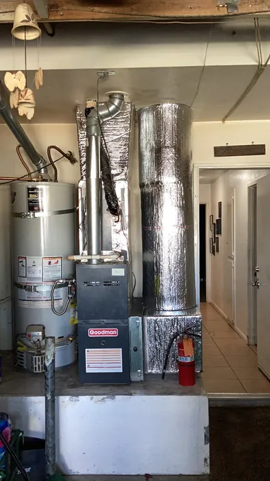 Goodman furnace with an insulated supply plenum next to a water heater inside a garage mechanical area in the High Desert.