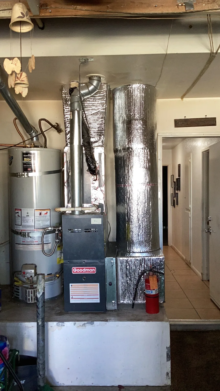 Goodman furnace with an insulated supply plenum next to a water heater inside a garage mechanical area in the High Desert.