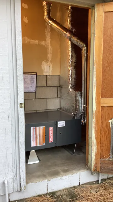 A newly installed Goodman gas furnace with copper line set and metal ductwork in an exterior utility closet of an Inland Empire home.