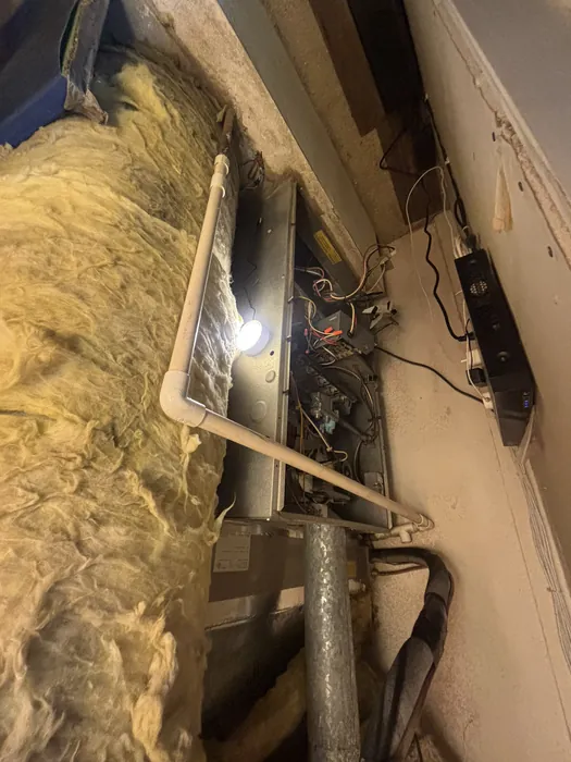 Horizontal furnace control board and blower section exposed during service in an insulated crawlspace with fiberglass batt insulation and a work light.