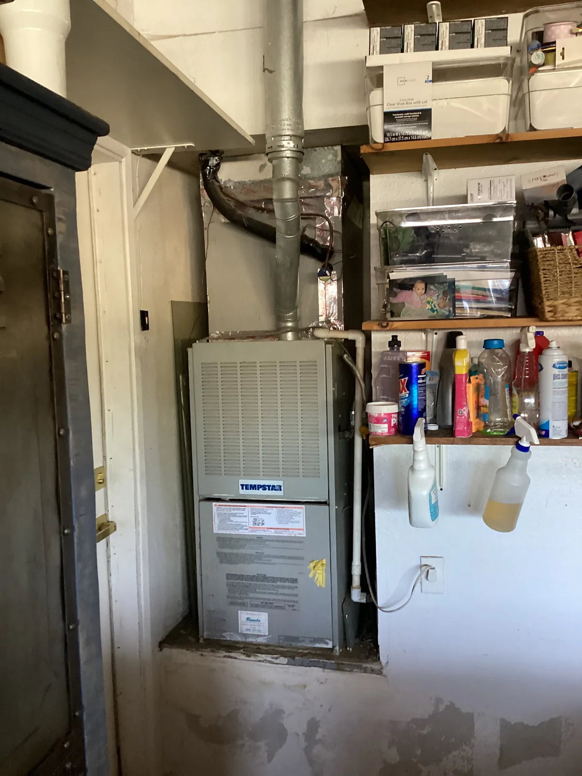 Tempstar gas furnace installed in an interior utility closet with flue venting and supply plenum next to household storage shelves.