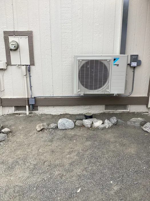 Daikin ductless mini split outdoor condenser mounted on a home wall with refrigerant line set, electrical disconnect, and conduit.