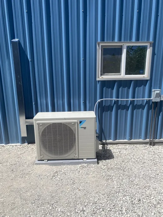 Daikin ductless mini-split condenser mounted on a wall bracket against blue metal siding outside an Inland Empire building.