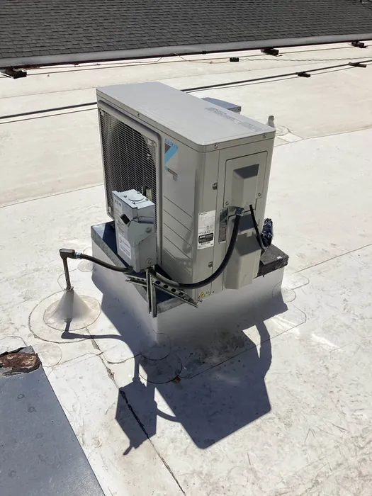 Daikin inverter mini-split condenser mounted on a roof curb with conduit and disconnect on a flat commercial roof in the High Desert.