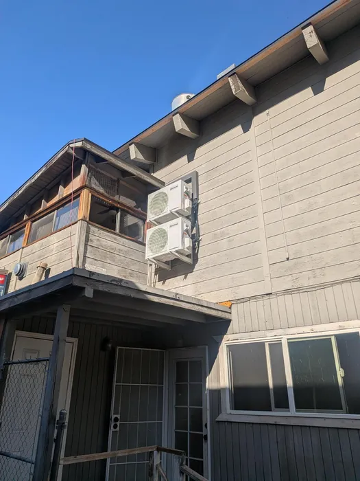 Two stacked mini-split condensers wall-mounted on a weathered two-story multifamily building under clear blue High Desert sky.
