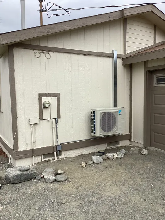 Wall-mounted ductless mini split condenser installed on the exterior of a manufactured home with refrigerant line set and disconnect.