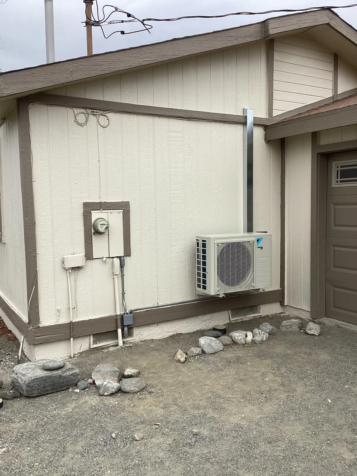Wall-mounted ductless mini split condenser installed on the exterior of a manufactured home with refrigerant line set and disconnect.