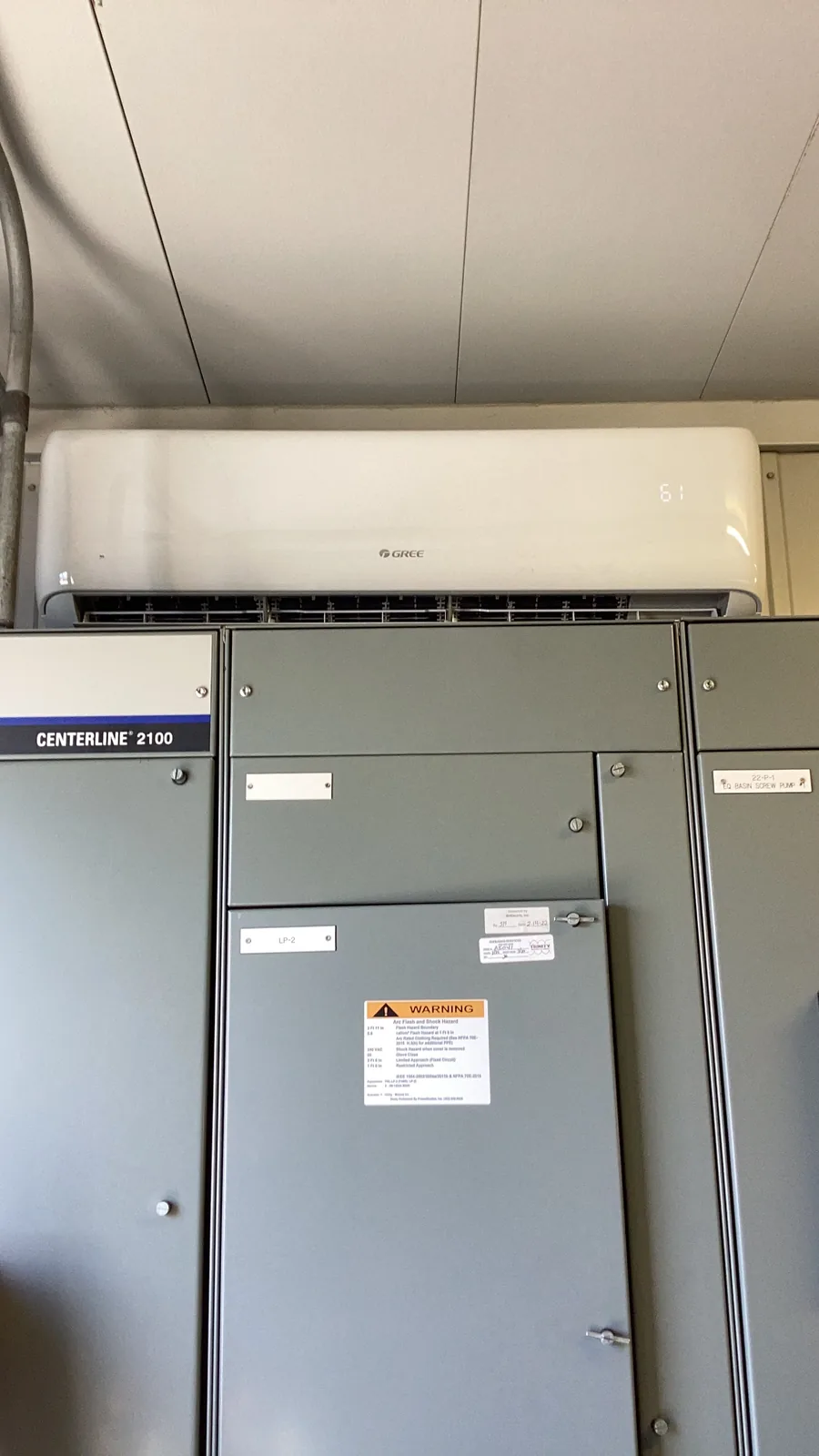 A Gree wall-mounted mini-split indoor head beside a gray Centerline air handler unit inside a mechanical room.
