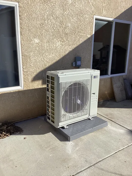 Front view of a wall bracket mounted mini split condenser fan grille and disconnect against a tan stucco wall outside a High Desert home