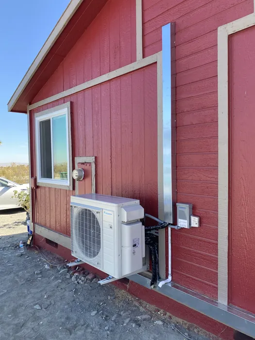 JC Energy Solutions mini split outdoor condenser unit installed against red siding next to a window on a High Desert home.