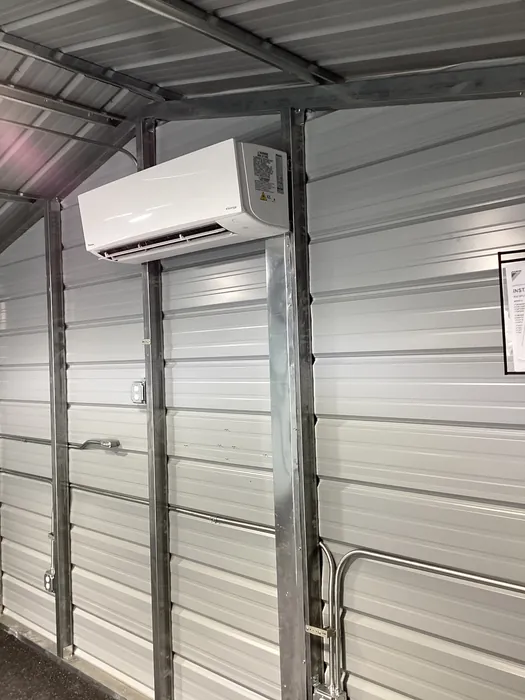 A white wall-mounted ductless mini-split air handler head mounted on steel framing inside a metal commercial building.