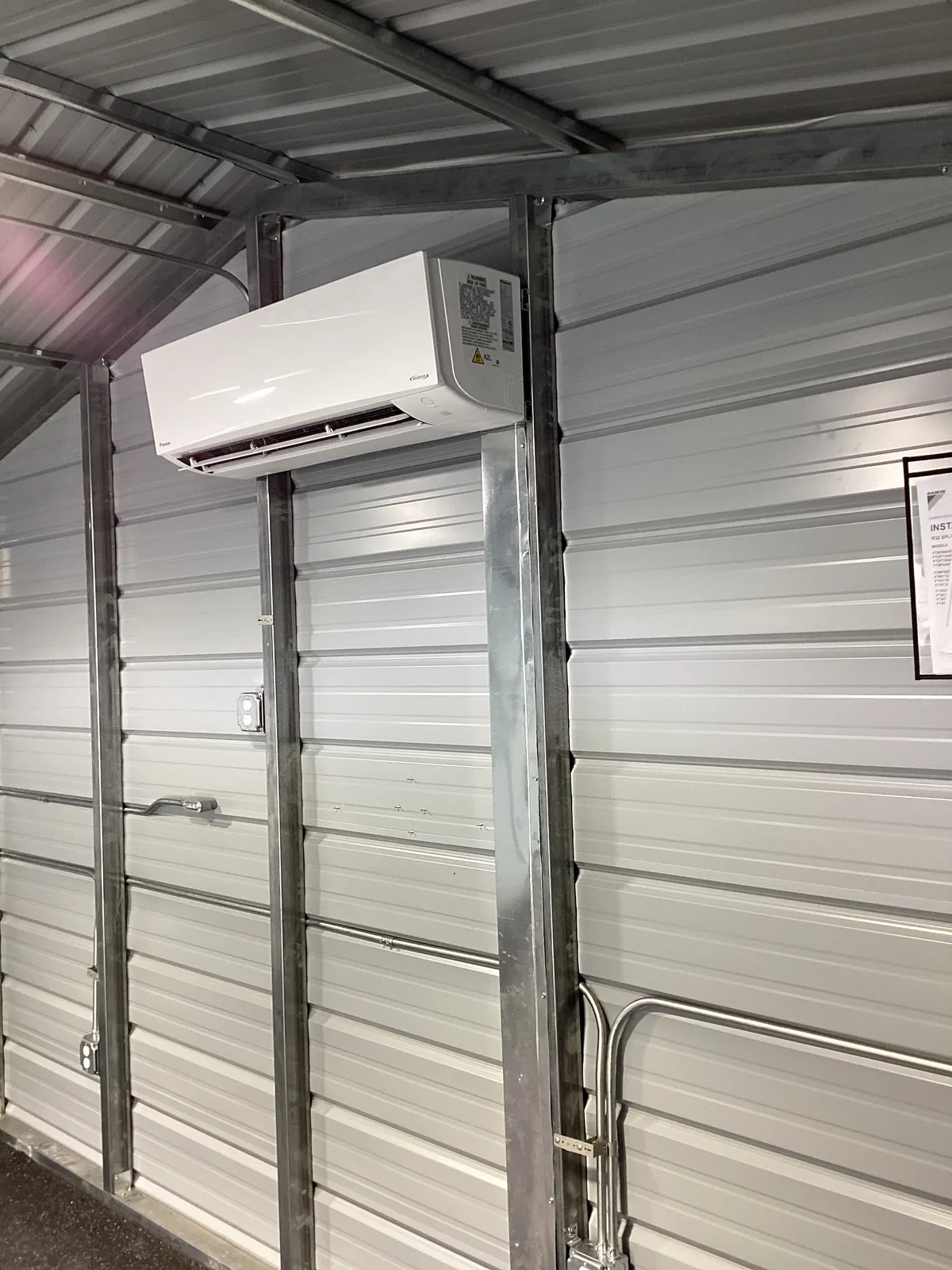 A white wall-mounted ductless mini-split air handler head mounted on steel framing inside a metal commercial building.