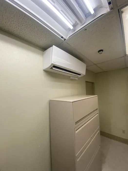 White wall-mounted Daikin ductless mini-split indoor head installed near the ceiling above a beige metal filing cabinet in a small office room.