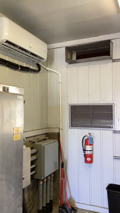 Indoor wall-mounted ductless mini-split air handler head beside a return grille and fire extinguisher in a High Desert mechanical room.